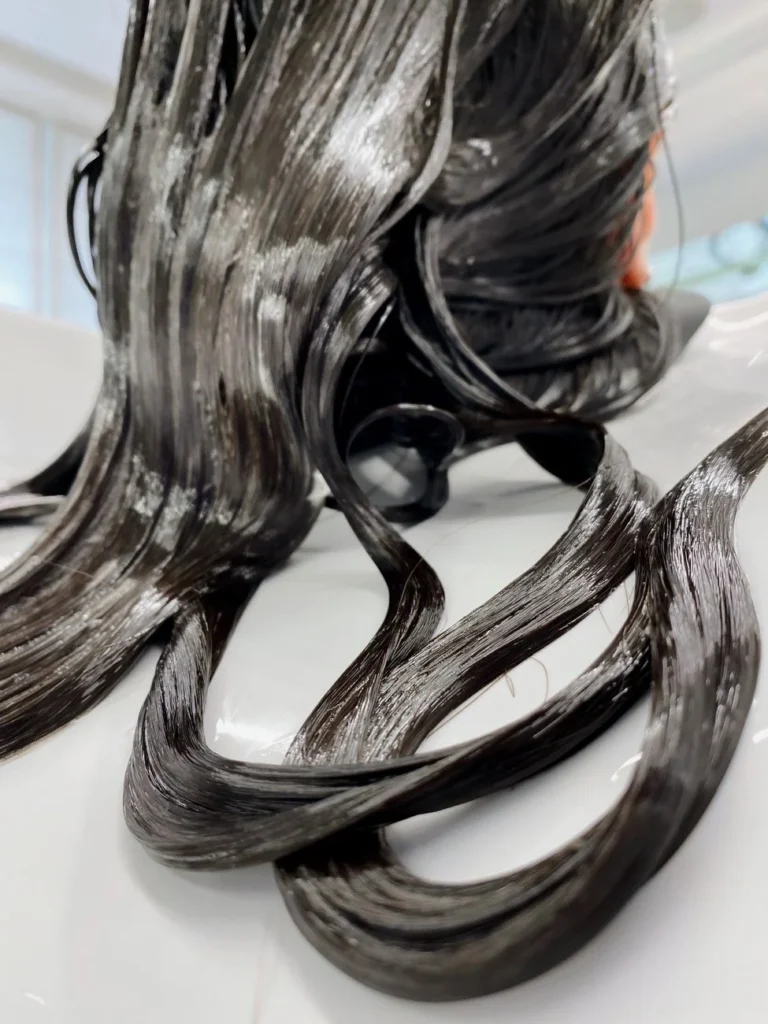 Close-up of brunette woman's wet hair receiving treatment at a salon.